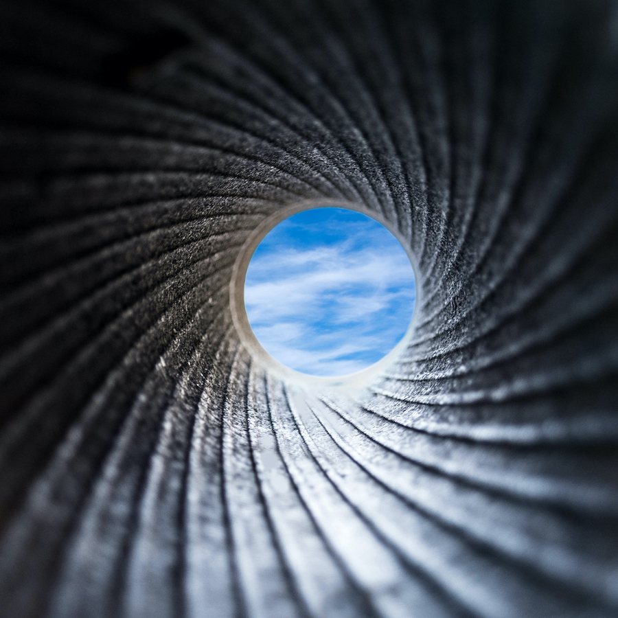 A view through a dark barrel of cannon to the blue sky with white fluffy clouds. Close up, selective focus. Abstract background concept